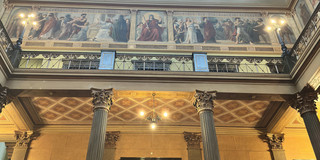 Courtyard of the University of Halle (Saale): A view looking up at columns, a door, busts in niches, historicist murals on the gallery, and an ornate coffered ceiling with blue panels.