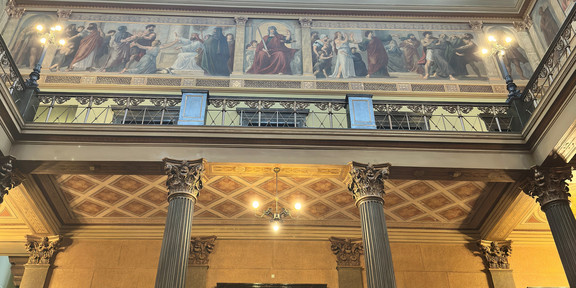 Courtyard of the University of Halle (Saale): A view looking up at columns, a door, busts in niches, historicist murals on the gallery, and an ornate coffered ceiling with blue panels.
