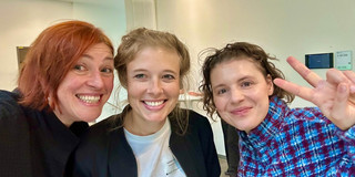Selfie von Dr. Katty Nöllenburg (links), Dr. Isabell Diekmann von der Universität Paderborn (Mitte) und Leonie Stoll (rechts) auf der DeZiM-Konferenz in Bielefeld. Die drei Frauen stehen eng beieinander und lächeln in die Kamera. Im Hintergrund ist ein heller Konferenzraum mit weißer Wand, Heizkörper und einem kleinen Display an der Wand zu sehen.