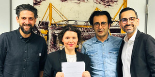 Vier Personen stehen nebeneinander vor einem Bild mit gelben Hafenkränen und blicken in die Kamera.