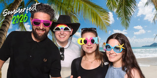 Vier Personen posieren gut gelaunt vor einer Strandkulisse mit Palmen und Meer. Sie tragen auffällige Partybrillen und Accessoires, unter anderem eine pinke Sonnenbrille, eine Regenbogenbrille, eine „COOL“-Brille und eine blaue Brille mit Seestern. Oben links steht „Sommerfest 2026“, unten rechts das Logo „ht Humanwissenschaften und Theologie“.