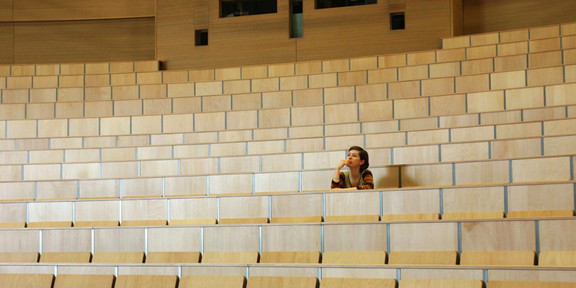 A student sits alone in a lecture hall at TU Dortmund University, gazing thoughtfully at the empty rows of seats.