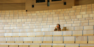 Studierende sitzt allein in einem Hörsaal der TU Dortmund und blickt nachdenklich über die leeren Sitzreihen.