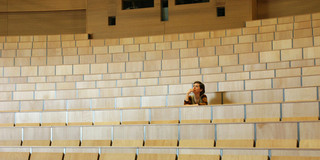 A student sits alone in a lecture hall at TU Dortmund University, gazing thoughtfully at the empty rows of seats.